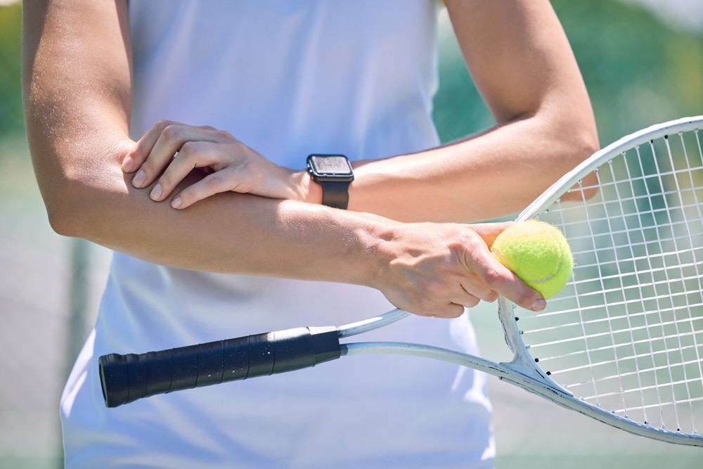 A view of a person holding thier elbow with pain along with a racket