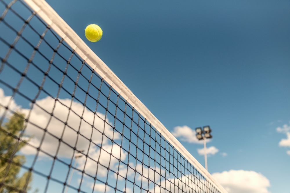 A view of a tennis net with a ball high up in the air