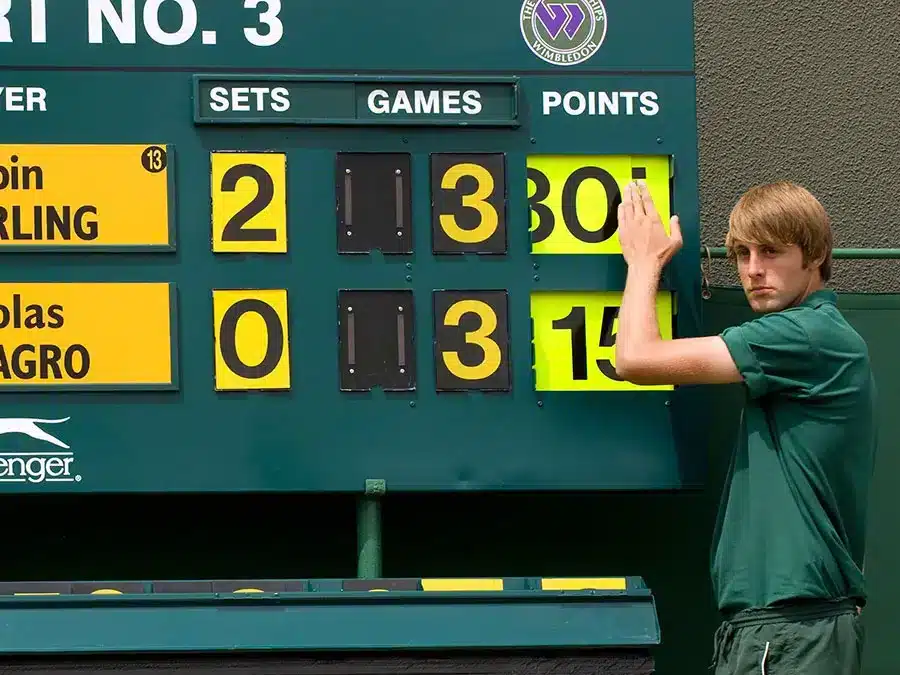 A view of a guy standing beside tennis scoreboard