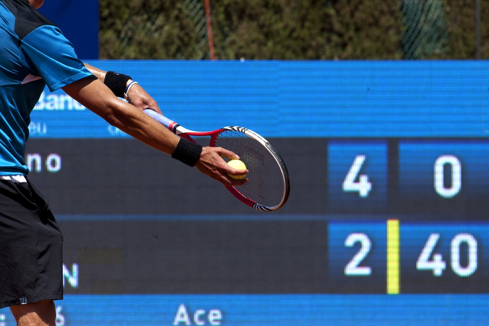 A view of a person hitting the tennis shot with a backdrop of score