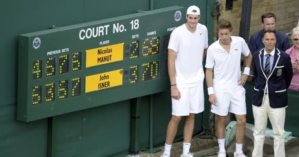 A view of professional tennis players standing beside a score board