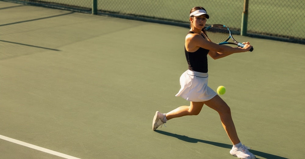 Woman playing tennis, showcasing a backhand shot with racket and ball on the court during a sunny holiday.