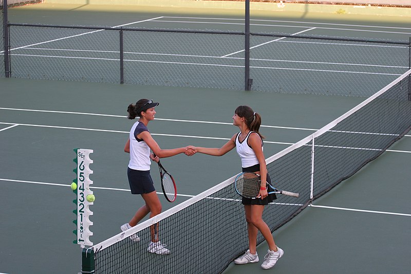 female players shaking hands on the court holding rackets in other hand