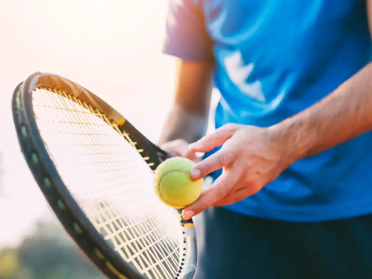 zoomed in view of amale hand holding a racket and tennis ball