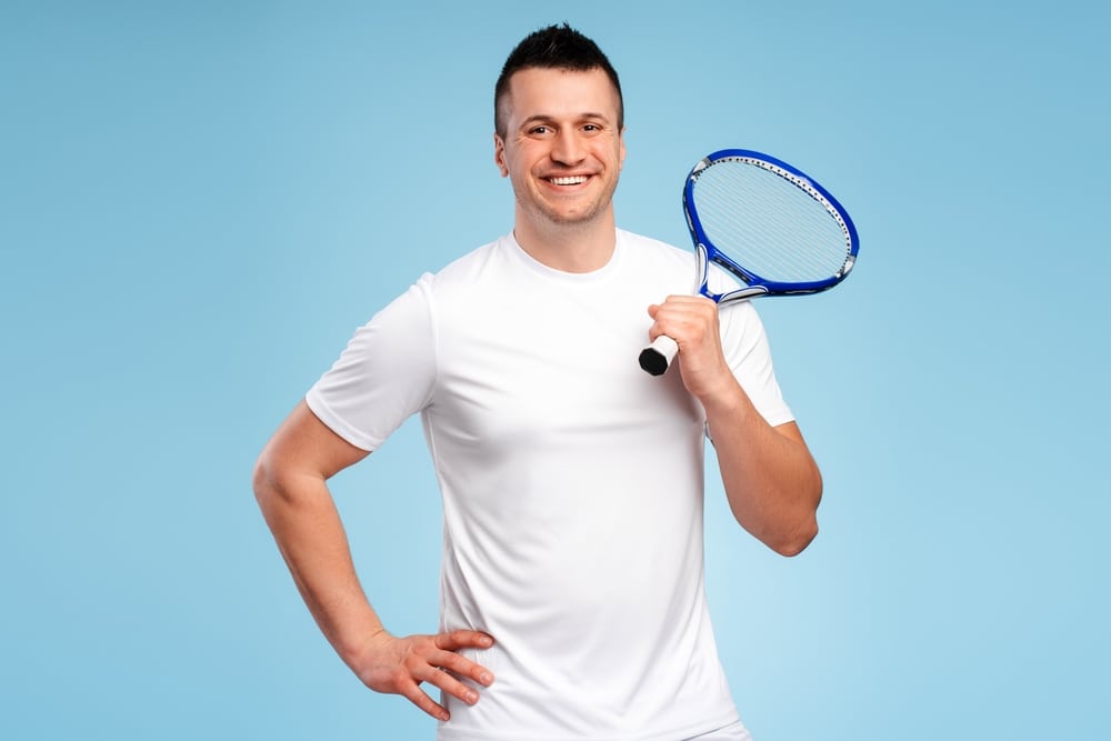 Confident Young Man In White Sportswear Holds Tennis Racket 